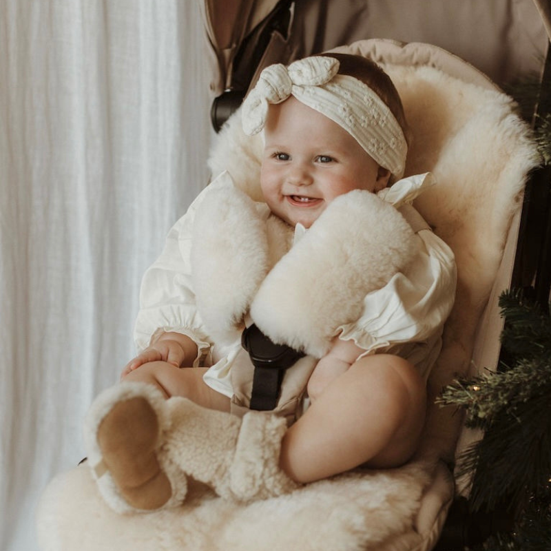 Sheepskin pram snuggler in pale white gender neutral shade in a joolz aer pram with a mum and baby next to it