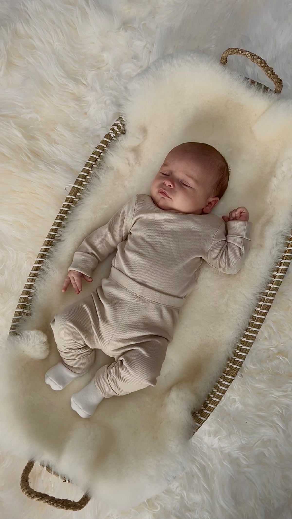 Newborn baby in a seagrass moses basket with a white sheepskin liner to help baby sleep