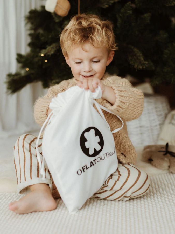 child holding FLATOUT bear gift bags by Christmas tree