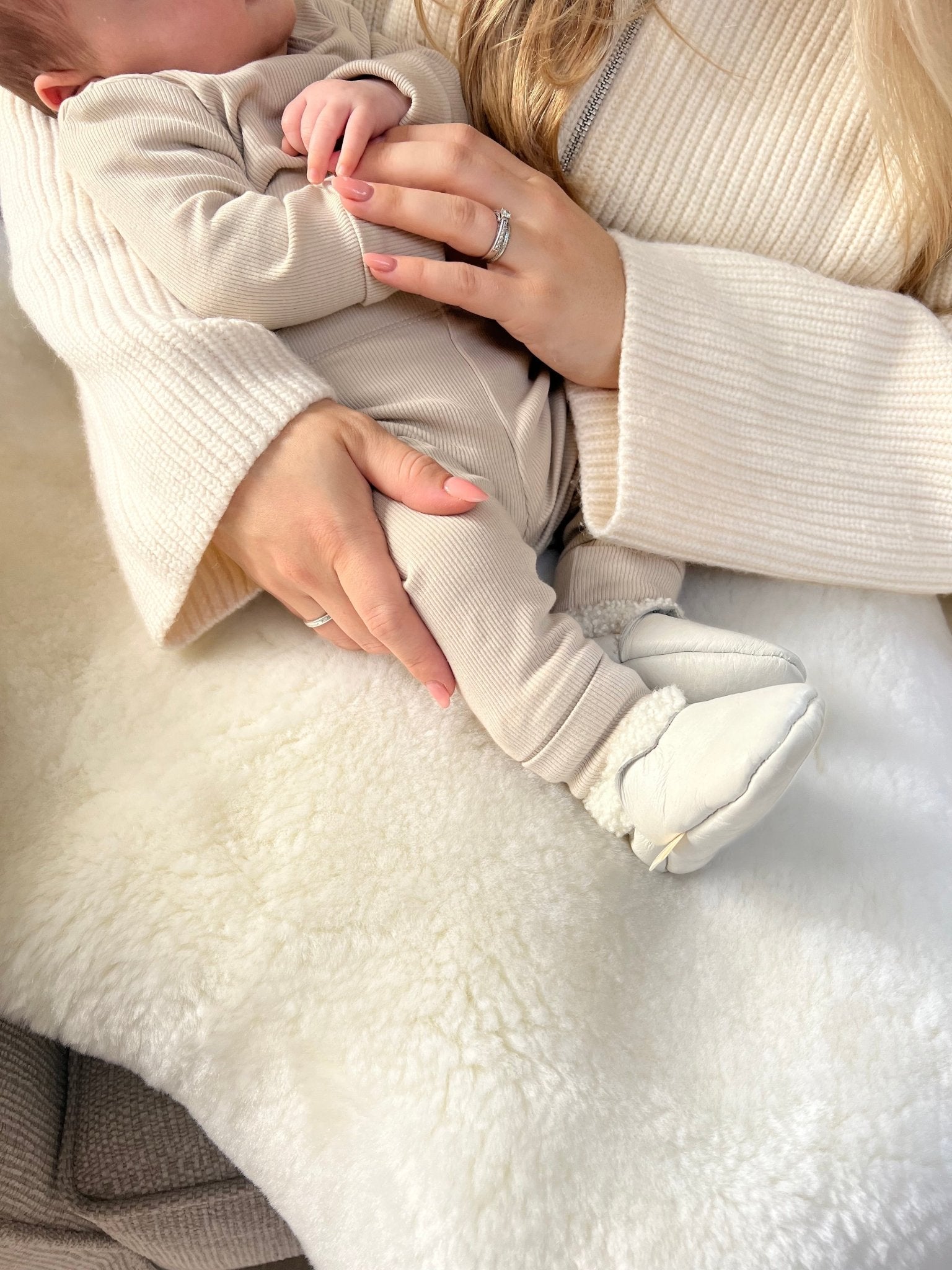 Newborn baby on a white sheepskin baby safe nursery rug wearing cream lambskin booties perfect for sensitive skin