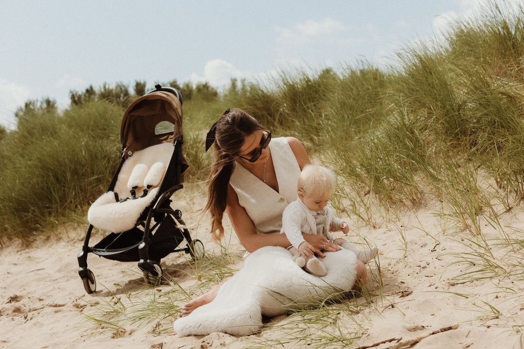 Mum and baby on beach with sheepskin rug and pram liner to keep cool