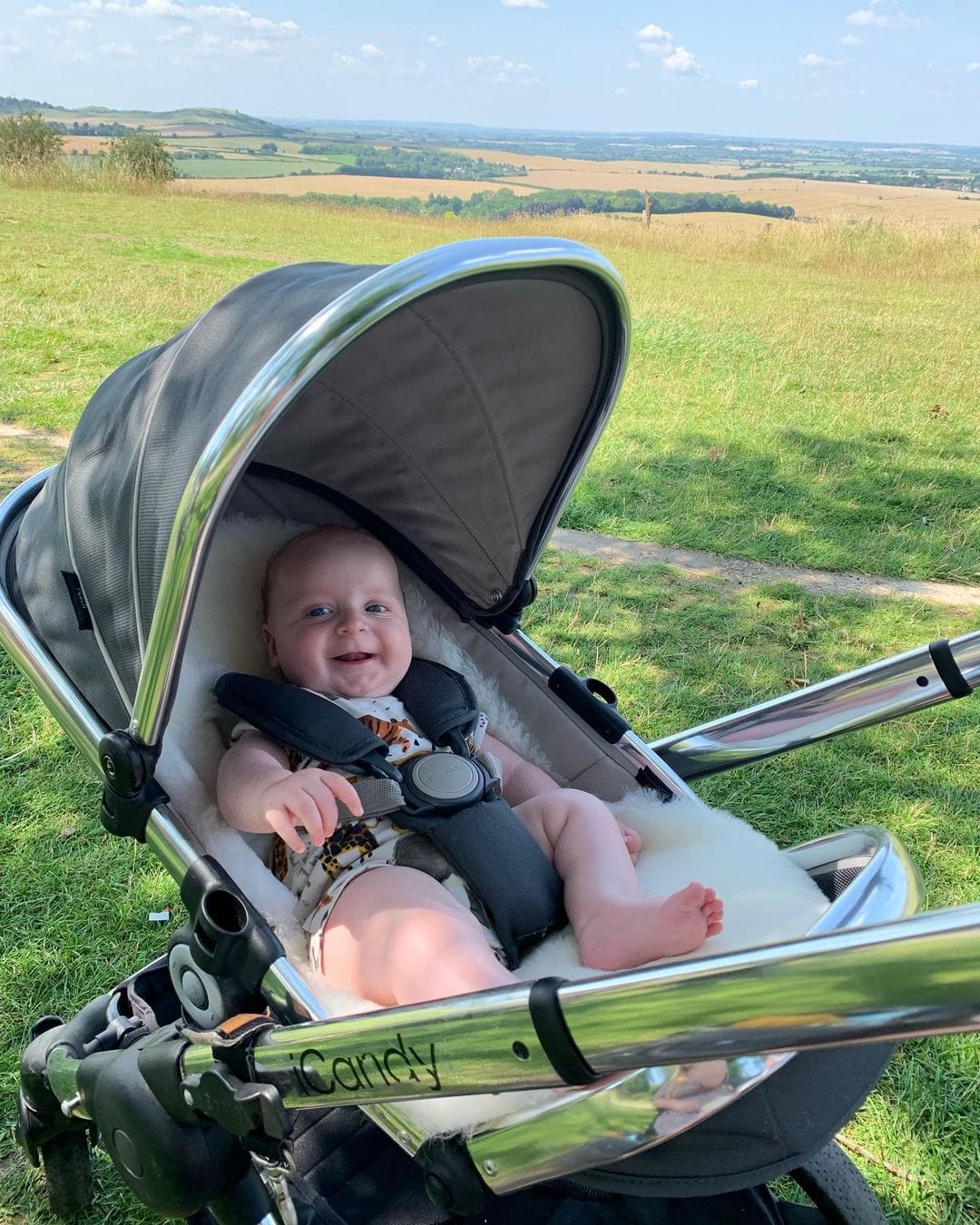 A smiling baby on a pram liner in an icandy peach pram in a field