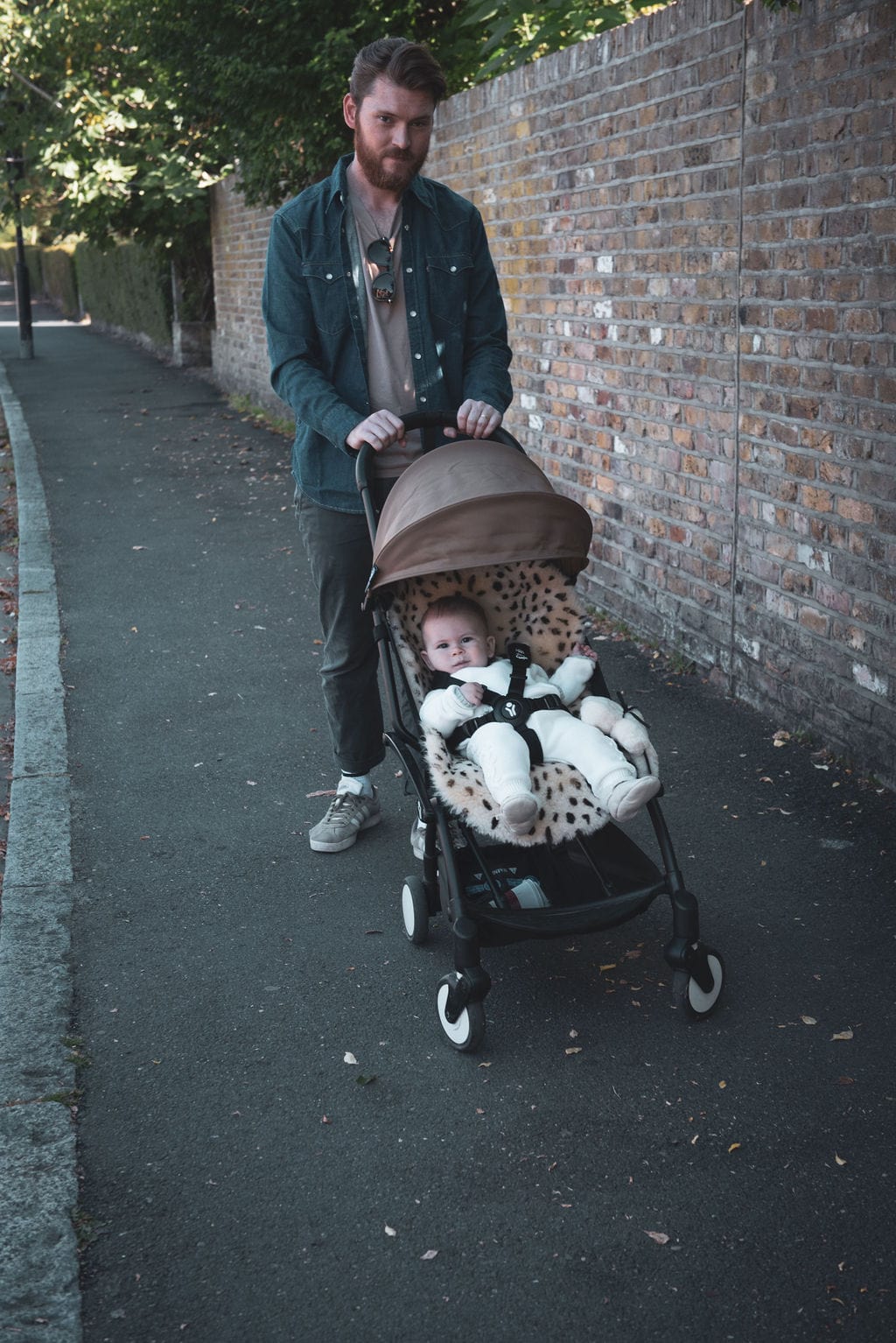 A man with a babyzen yoyo pram with a leopard print sheepskin liner and a baby