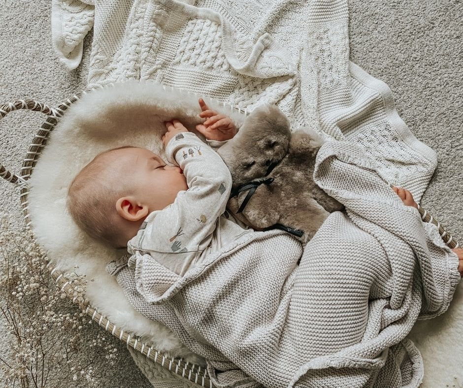 baby asleep in a sheepskin lined  moses basket with sheepskin flatout teddy bear in gender neutral latte