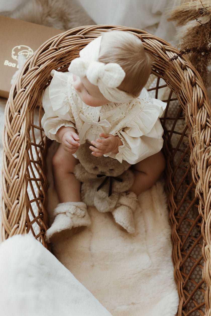 Newborn crib with baby holding flat teddy bear and teddy merino boucle booties, laying on a sheepskin carrycot liner