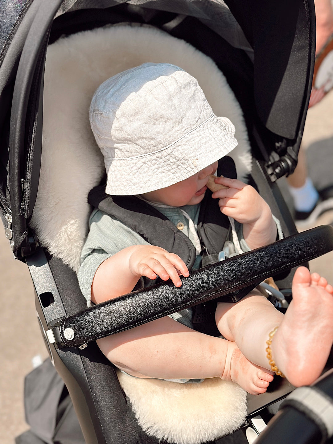 Baby in pram with a sheepskin pram liner which is breathable and thermostatic keeping baby cool