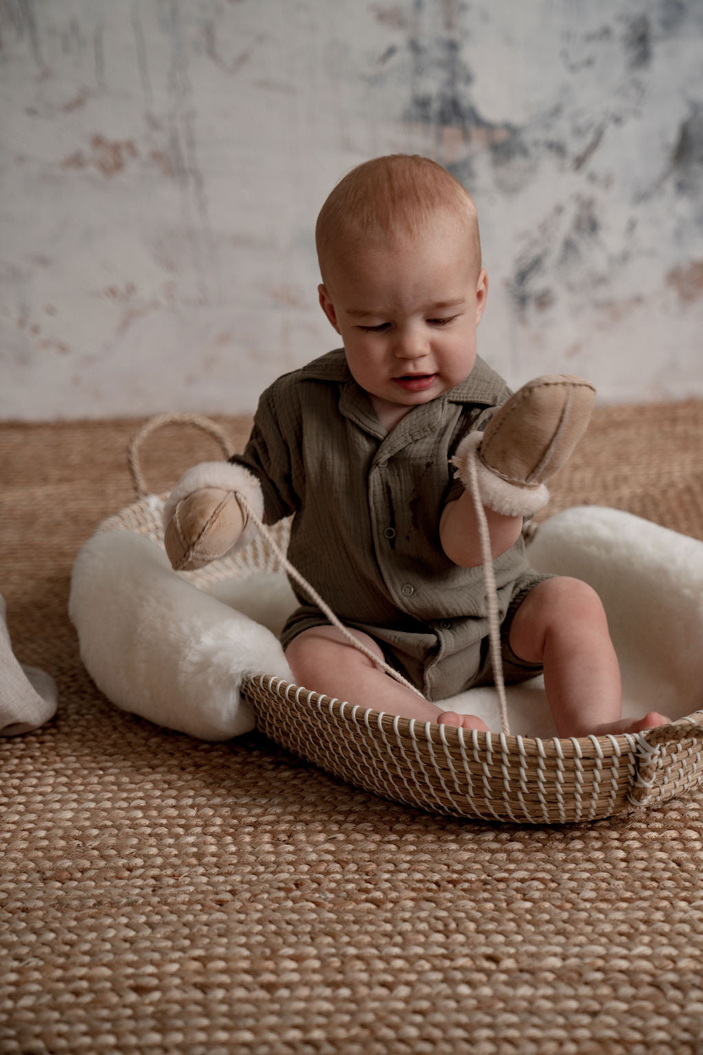 Baby in a moses basket with a sheepskin bassinet liner and weary puddy mittens on string