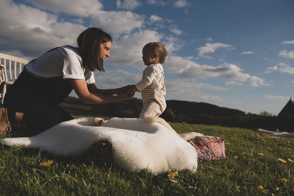 Toddler standing on a white sheepskin rug with mum in a meadow
