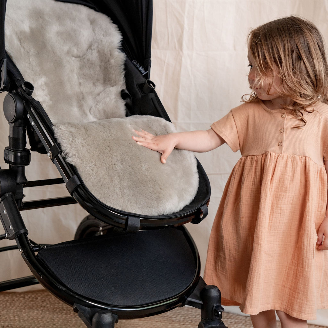 Pale Brown Natural Shorn Lambskin Bugaboo™ Pram Liner for Comfort and Sleep, a toddler stroking the soft sheepskin