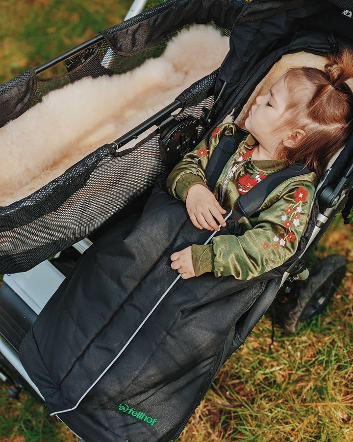 Toddler asleep in a mountain buggy pram wrapped in a cosy sheepskin footmuff to keep her warm