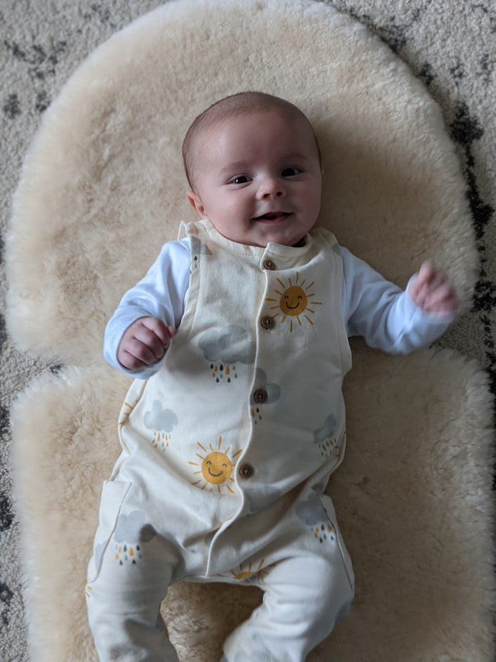 Baby on a natural honey sheepskin pram liner in the nursery enjoying play time