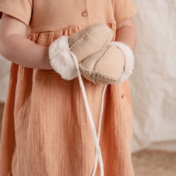 A little girl wearing neutral mittens on string