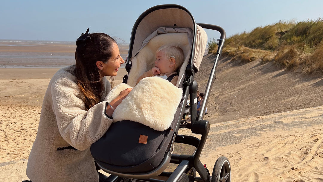 Baby in a sheepskin pram footmuff on the beach with milk merino lining and keeping baby warm in the cold