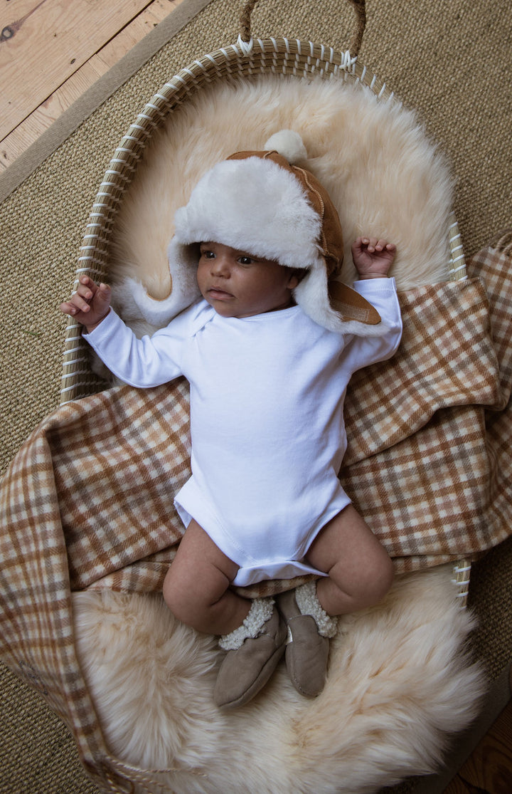 Gender neutral sheepskin soft liner for a bassinet with a newborn baby laying on it