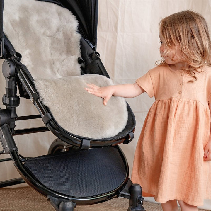 Pale Brown Natural Shorn Lambskin Bugaboo™ Pram Liner for Comfort and Sleep, a toddler stroking the soft sheepskin